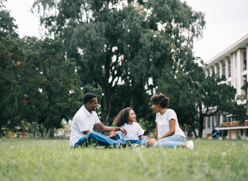 A Black family sits in a grassy park having a picnic